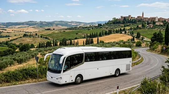 Pullman Gran Turismo bianco e rosso che percorre una strada panoramica tra colline toscane con vigneti e cipressi, sotto la luce dorata del tardo pomeriggio primaverile